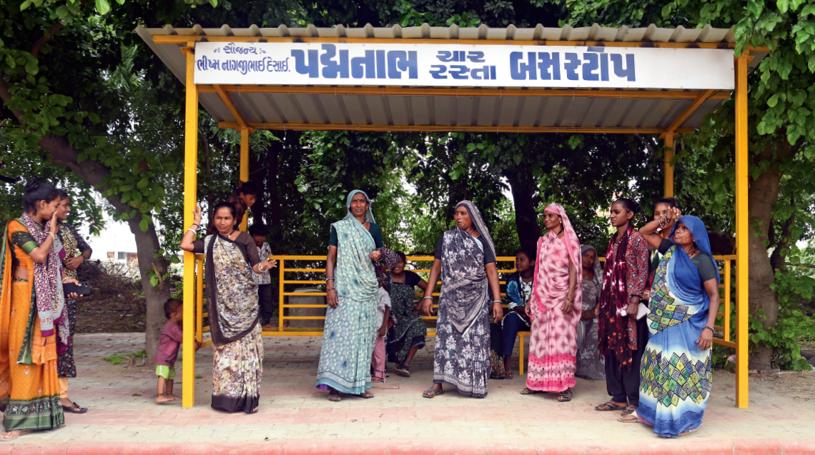Women wait at a bus stop in Patan where overhead sprinklers keep commuters cool