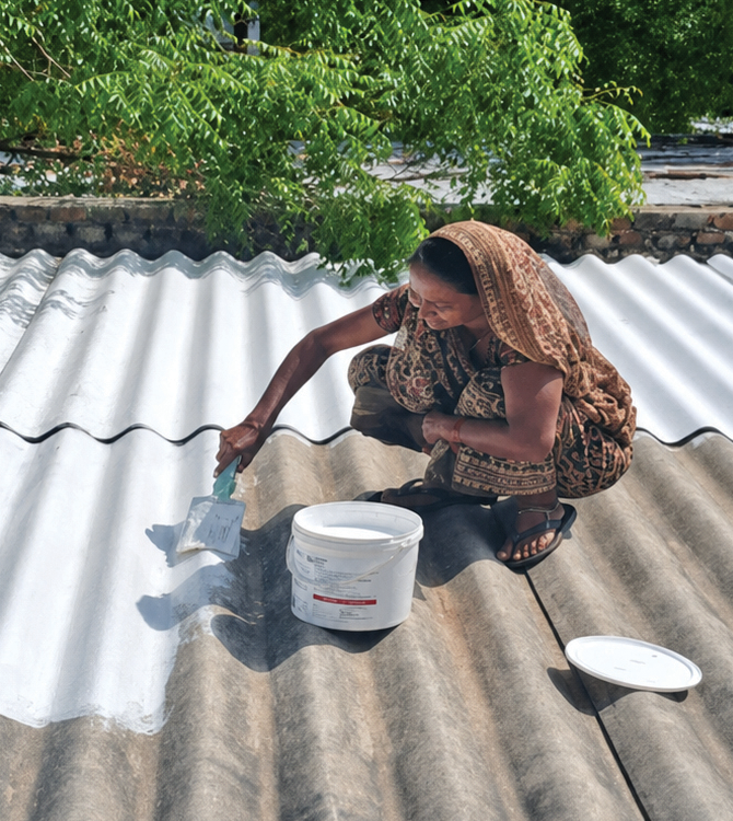 A resident of Bhattiwada in Patan applies white solar reflective index paint to the roof of her house to cool it
